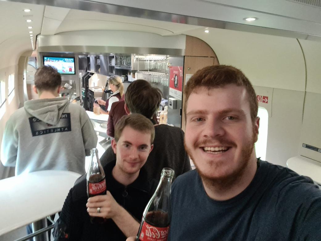 Zwei Teilnehmende im Boardbistro der Bahn mit einem Getränk in der Hand