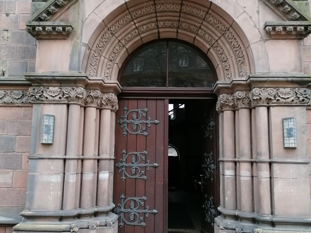 ein Sandsteinportal mit geöffneter Tür. Darüber das PX