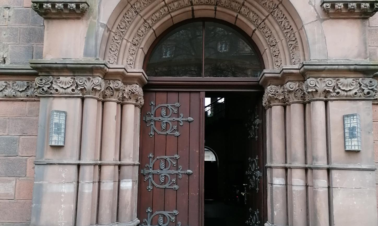 ein Sandsteinportal mit geöffneter Tür. Darüber das PX